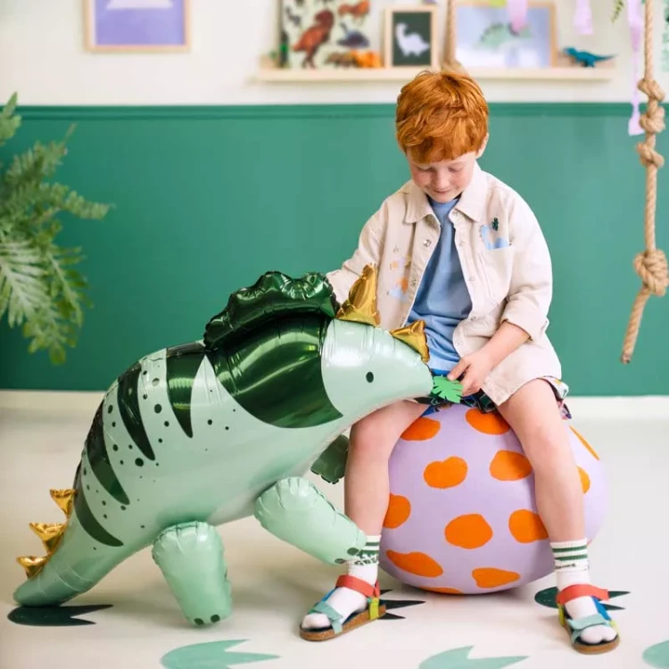Zbliżenie na elementy zestawu - sztućce, książeczkę i album z motywem uroczego dinozaura i pastelowych balonów.