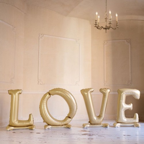 Złoty balon foliowy tworzący napis LOVE ustawiony w jednym rzędzie jako dekoracja ślubna.