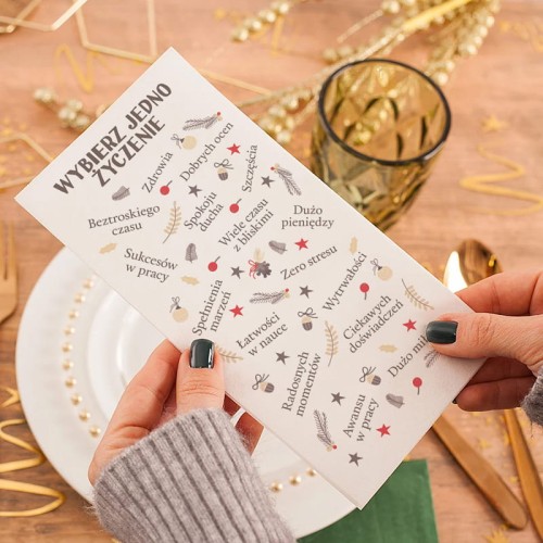 Ręka trzymająca opłatek z nadrukowanymi życzeniami świątecznymi przed rozpoczęciem kolacji wigilijnej.