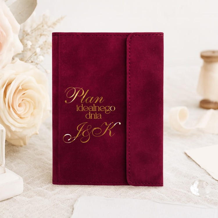 Planer ślubny z weluru z inicjałami pary młodej na tle dekoracji.