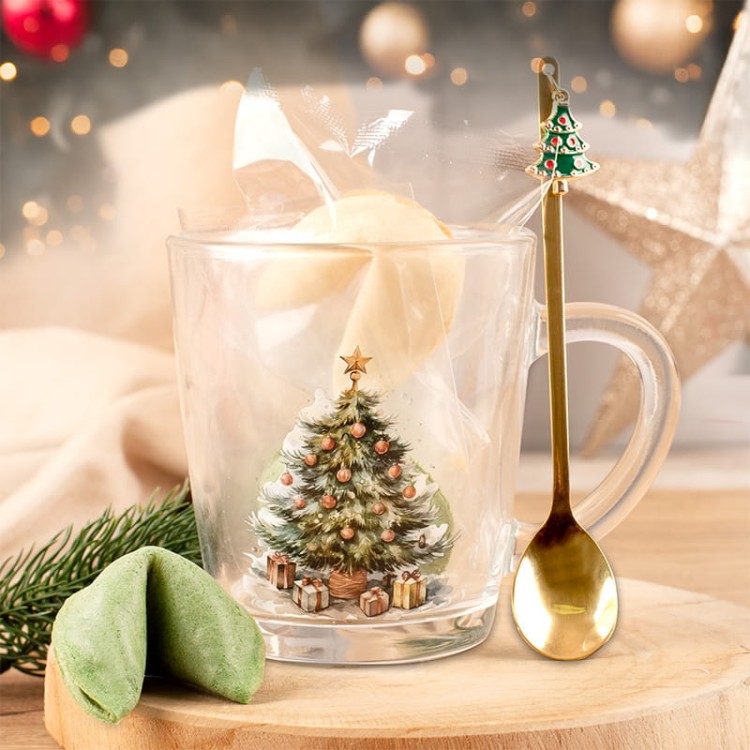 Szklanka z grafiką świątecznej choinki, ciasteczkiem z wróżbą i złotą łyżeczką.