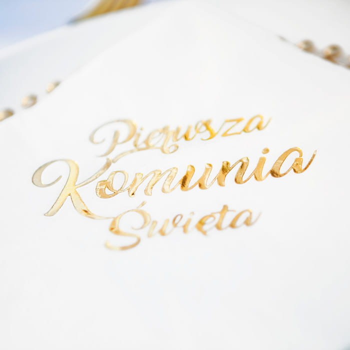 Wytłaczany, złoty napis Pierwsza Komunia Święta na serwetce.