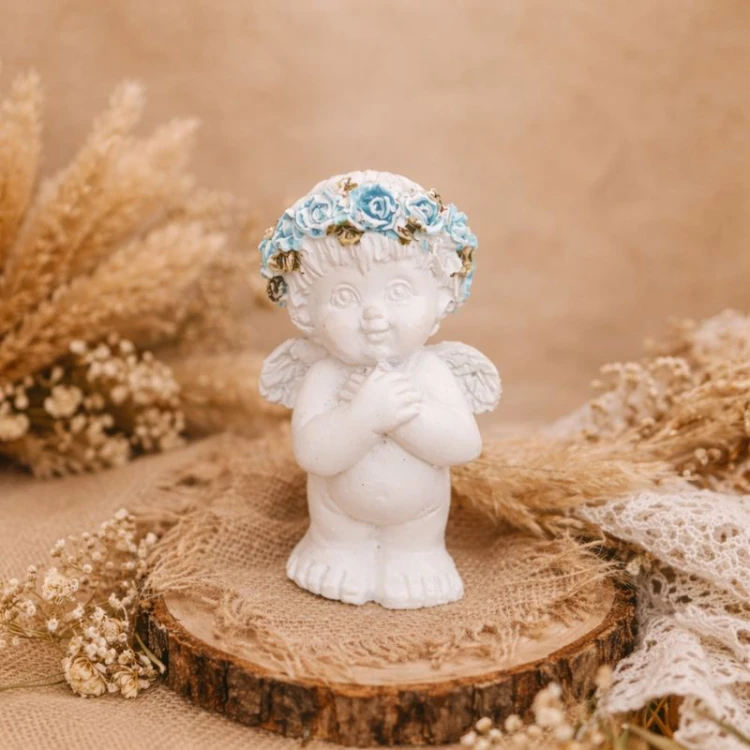 Biały aniołek z niebieskim wiankiem na głowie.