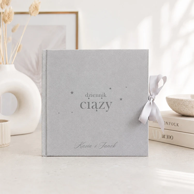 Personalizowany album ciążowy w szarej welurowej oprawie ustawiony w jasnym wnętrzu.