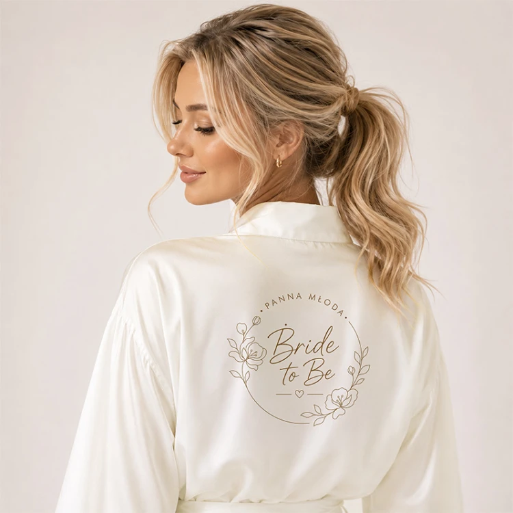 Nadruk Bride to Be na białym satynowym szlafroku dla Panny Młodej.