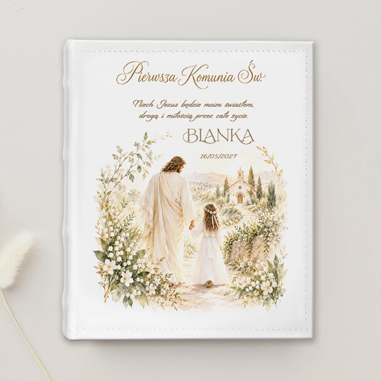 Personalizowany album komunijny dla dziewczynki przedstawia Jezusa prowadzącego dziecko w stronę kościoła.